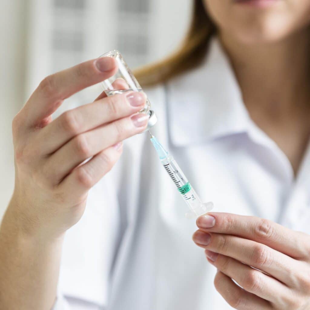 A person in a white lab coat filling a syringe with liquid from a vial.