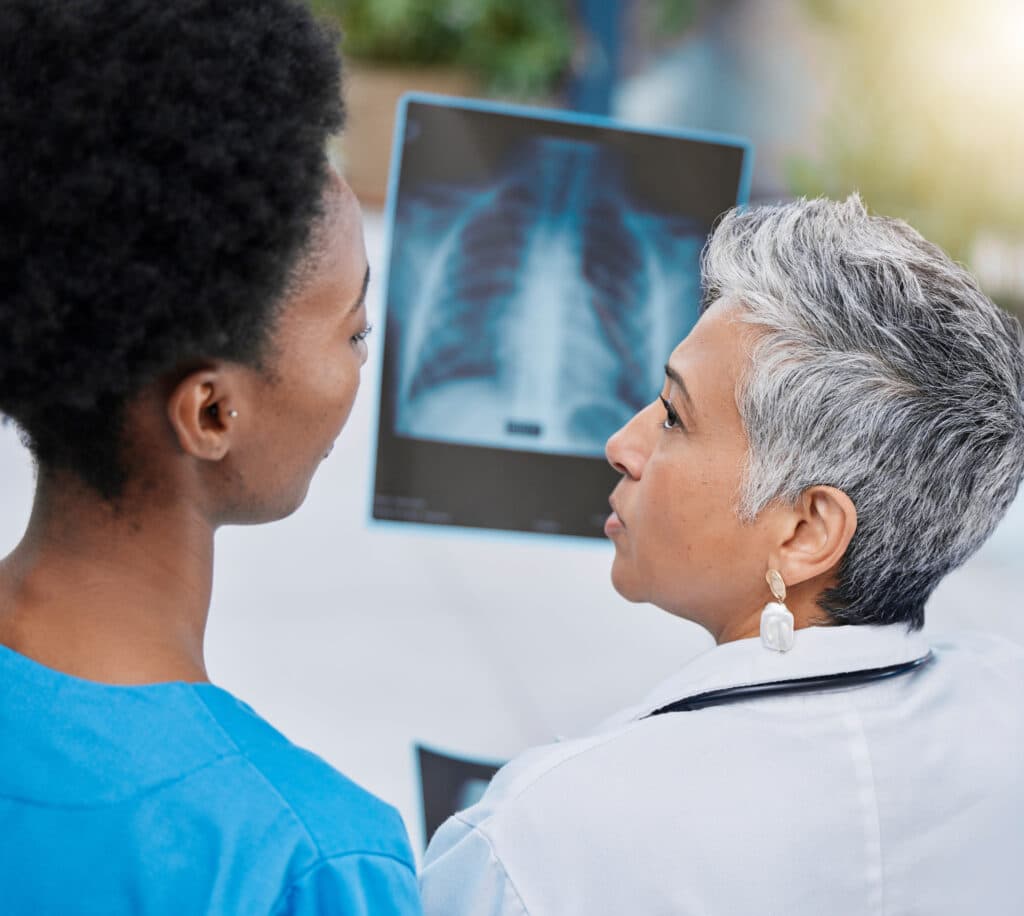 Two medical professionals examine a chest X-ray displayed on a screen, discussing the findings.